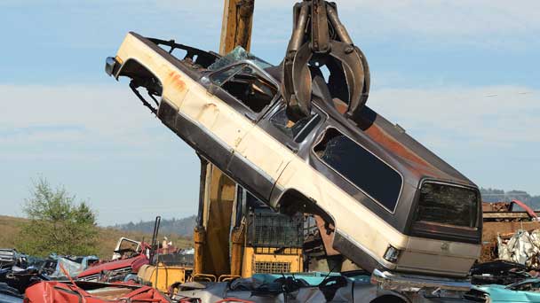 Large equipment handling old and junk car on a wrecking yard.